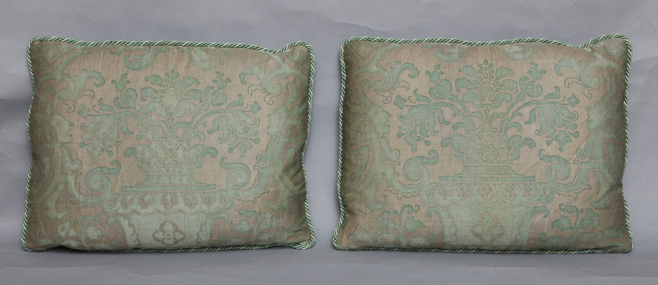 A pair of Fortuny fabric rectangular cushions with antique silver ground damask Carnavalet design, pale green silk backs, and braided edging.