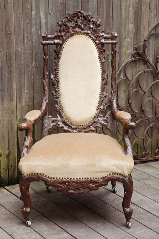 An Austrian Black Forest open armchair with canted back having open fret design with inset oval upholstered panel, the hand carved walnut frame in a naturalistic style suggesting tree branches with carved details on the arched crest, legs, and