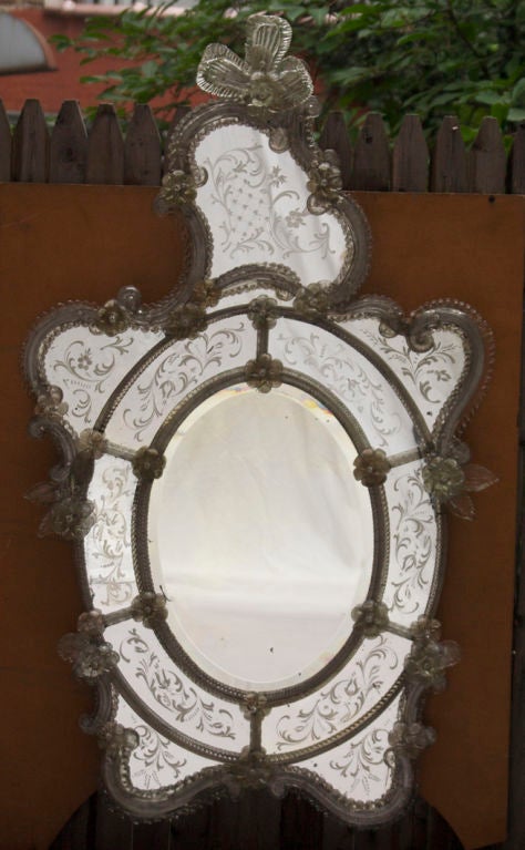An Italian Rococo Venetian glass mirror with oval beveled center glass surrounded by hand blown Murano glass elements secured by floral rosettes, the asymmetrical crest with etched mirror section.