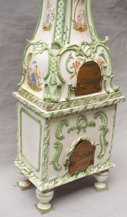 An Italian porcelain terra cotta stove, the square base supported by turned porcelain legs with square plinths. The upper section with Rococo shaped front and sides having Chinoiserie motif decoration with palm trees, floral decoration, scrolls, and