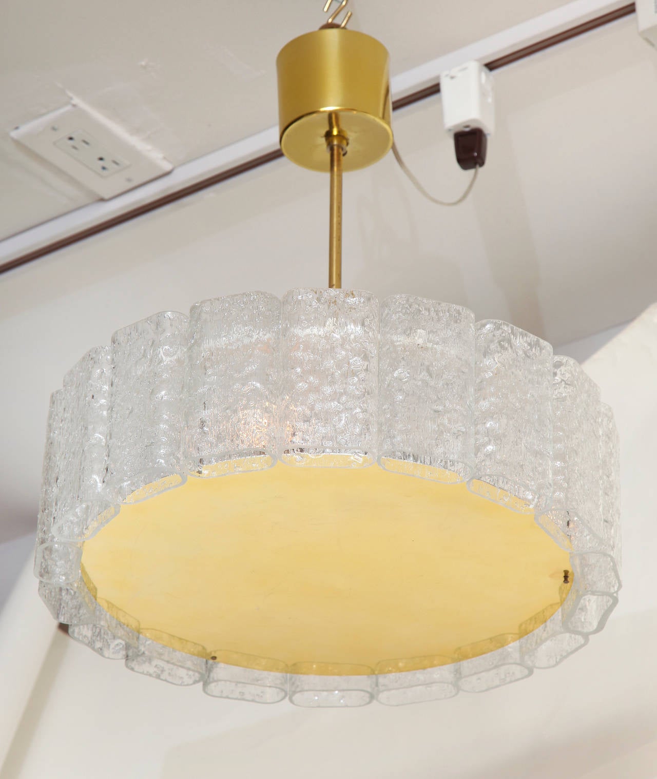 A contemporary design ceiling fixture with glass cylinders. The flat polished brass disc on underside surrounded by textured oval glass cylinders.