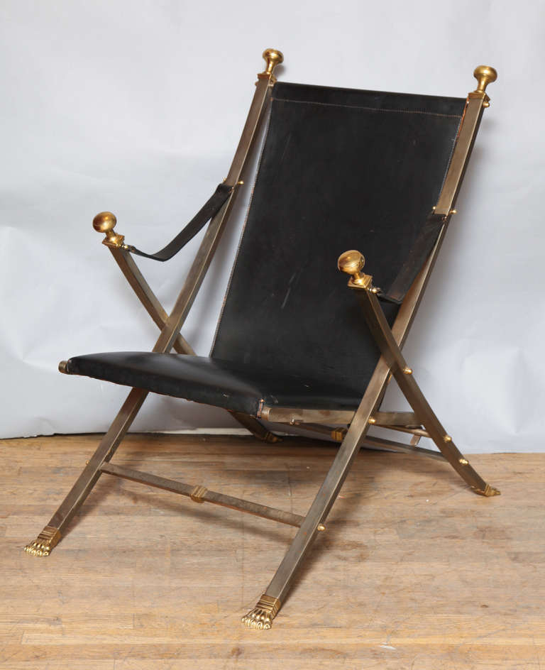 A Jansen-style campaign chair, the x-shaped frame with leather upholstered seat and back. The steel frame accented with brass lines, paw feet, and finials.