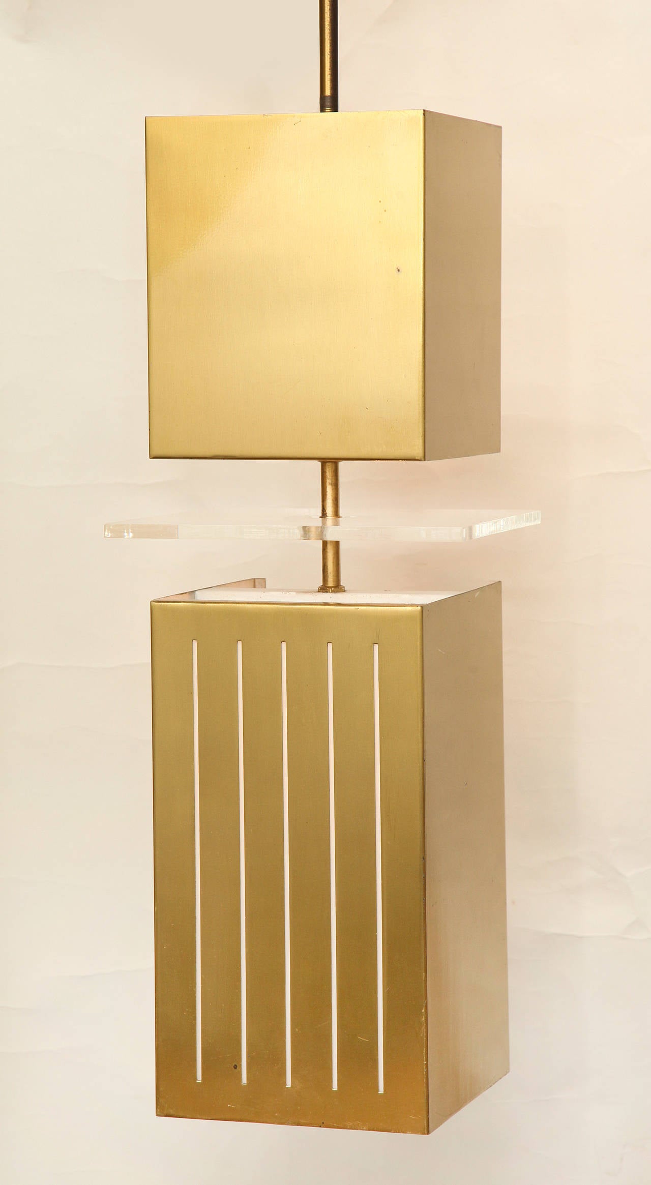 A pair of Mid-Century bronze square pendant lights. The lower section with vertical slits emitting light from an interior socket and illuminating a square floating plexi disc between upper and lower sections, suspended from rod and canopy. Minimum