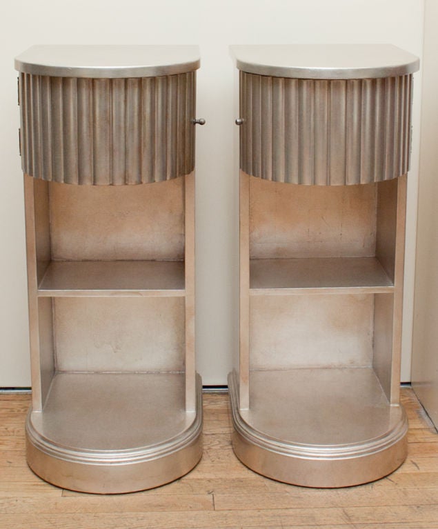 A pair of 3 tiered American Art Deco bedside tables rounded fronts, the upper section with drawer having vertical fluted edge opening to the right or left to reveal storage. The surfaces with silver leaf in square sections. Finish restored. Signed