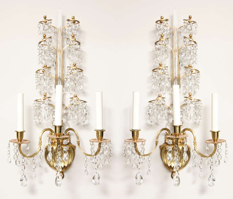 A pair of three light bronze Baltic-style wall sconces. The backplate with carved rounded glass. Vase shaped center secured by bronze leaf tip ornaments below crystal obelisk surrounded by four tiers of inswept scrolling arms, draped with crystal
