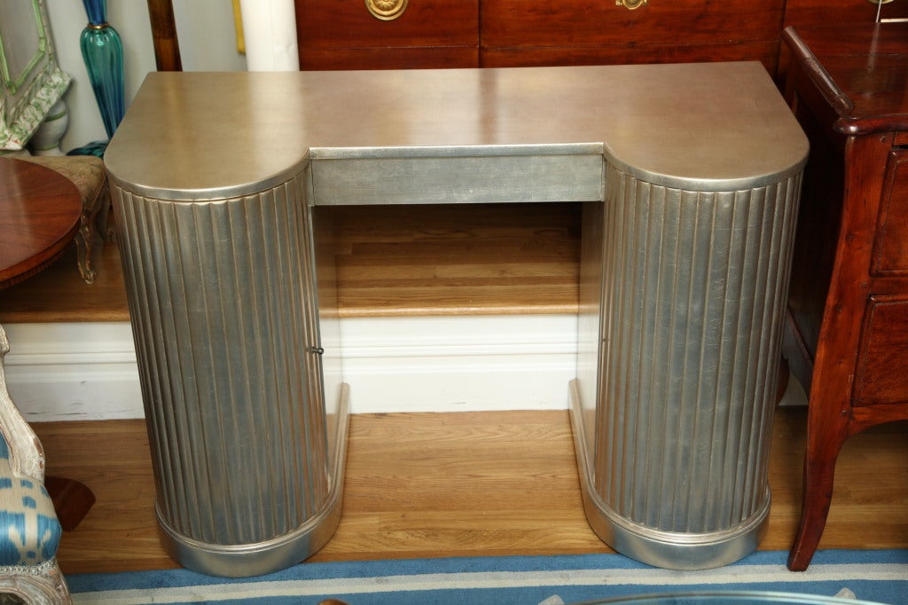 An American Art Deco dressing table with open kneehole below apron fitted with drawer.  The front of each side with rounded reeded cabinet door fronts finished with Silver leaf and square sections over all by American maker Kittinger.