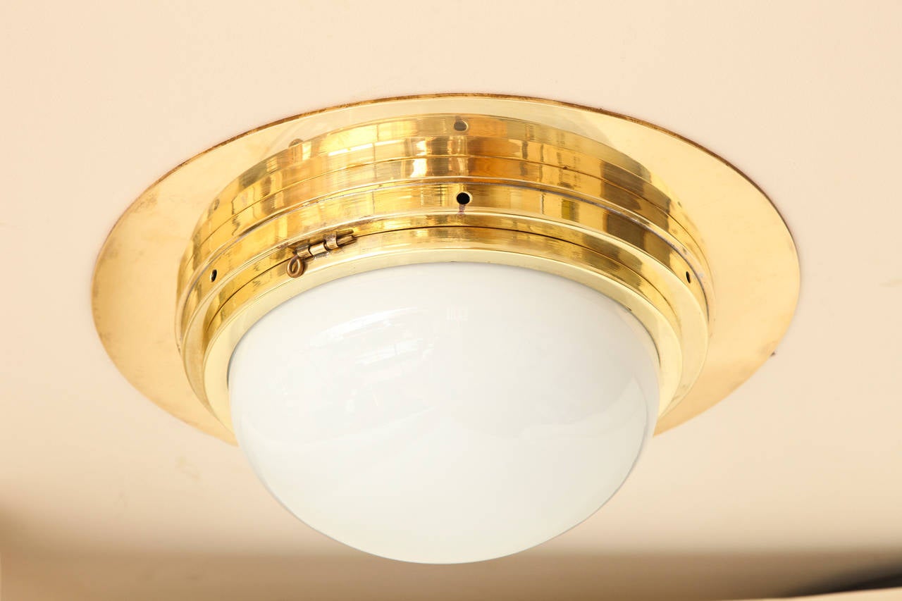 A round bronze flush mounted ceiling fixture with half dome glass. The stepped ceiling mount with hinged frame securing white opaline glass dome concealing two electric sockets.