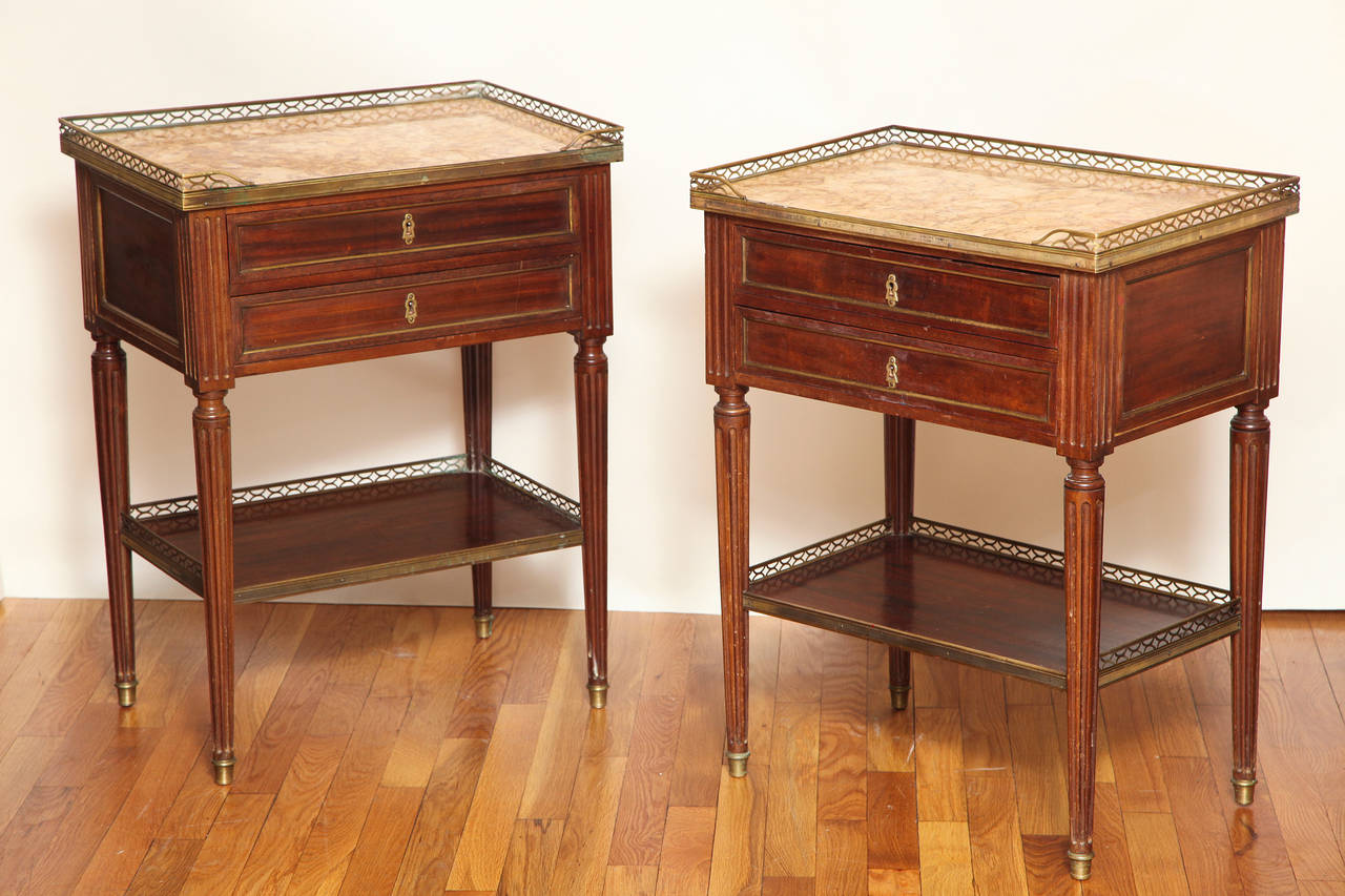 A pair of French Louis XVI style two drawer bed side tables. The drawer fronts, backs and sides having recessed panels framed with brass molding. The marble tops having bronze edging and metal gallery on three sides. The four round tapering fluted