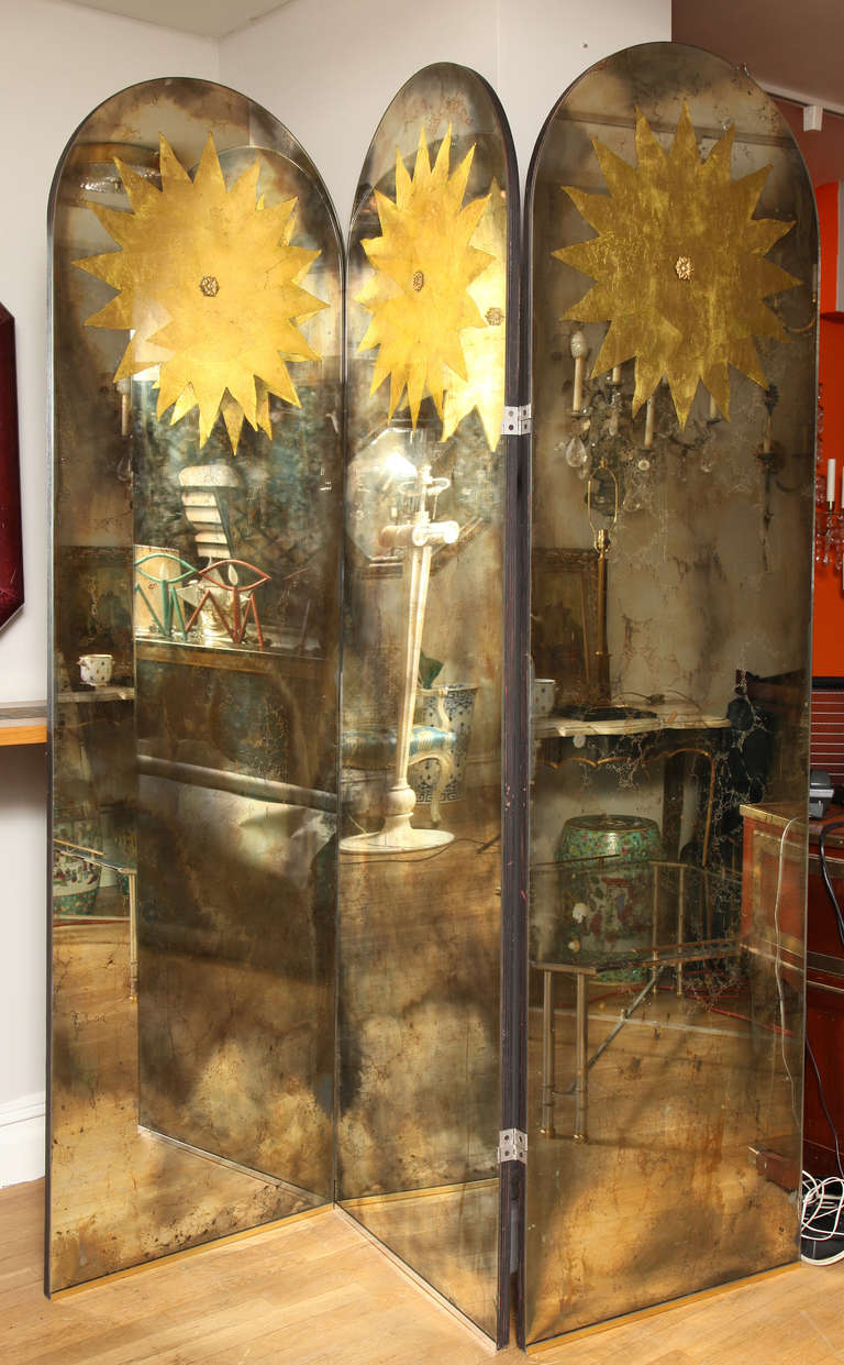 A three panel American mirrored screen. Each panel with arched top above reverse glass decorated sunburst motif in gold.