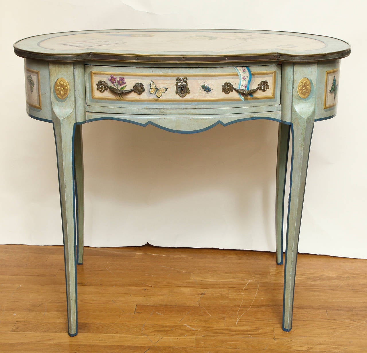 A French Transitional style (Louis XV - Louis XVI) kidney shaped writing table with single drawer in apron having bronze pulls. The painted decorated surfaces having ivory reserves within blue green cross banding and expertly panted trompe l'oeil