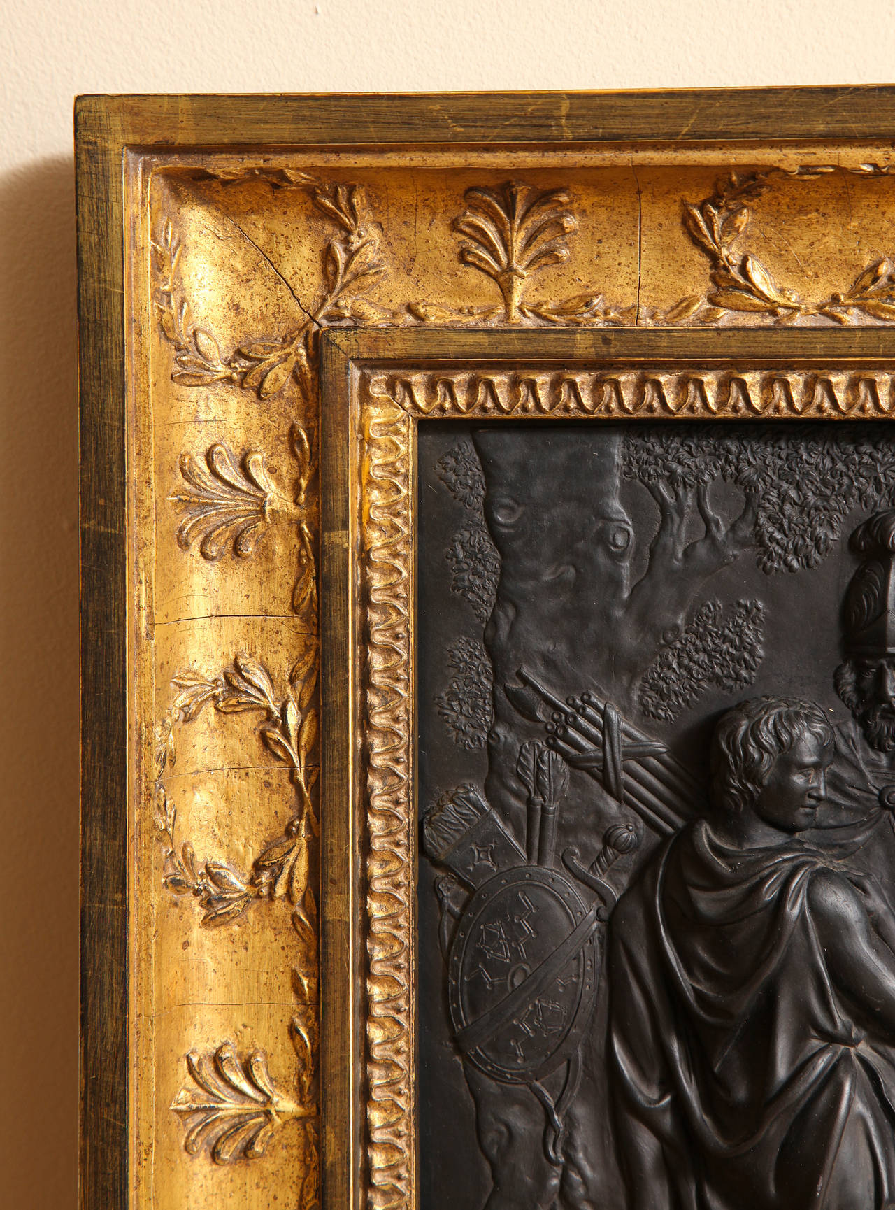 A black basalt Wedgwood plaque from the estate of Bill Blass depicting a procession of Classical figures after battle in low relief; now framed with carved and gilt wood Empire design, rectangular custom carved in gilt wood, Empire design;