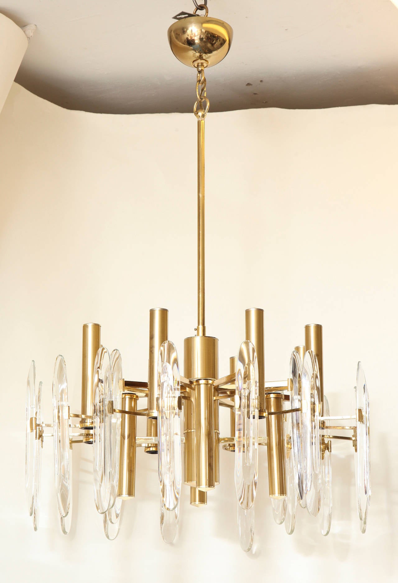 An American contemporary design 12-light chandelier with brushed finished matte brass frame having lights within acrylic spear shaped elements with rounded ends interspersed among brass cylindrical elements issuing light from above and below.