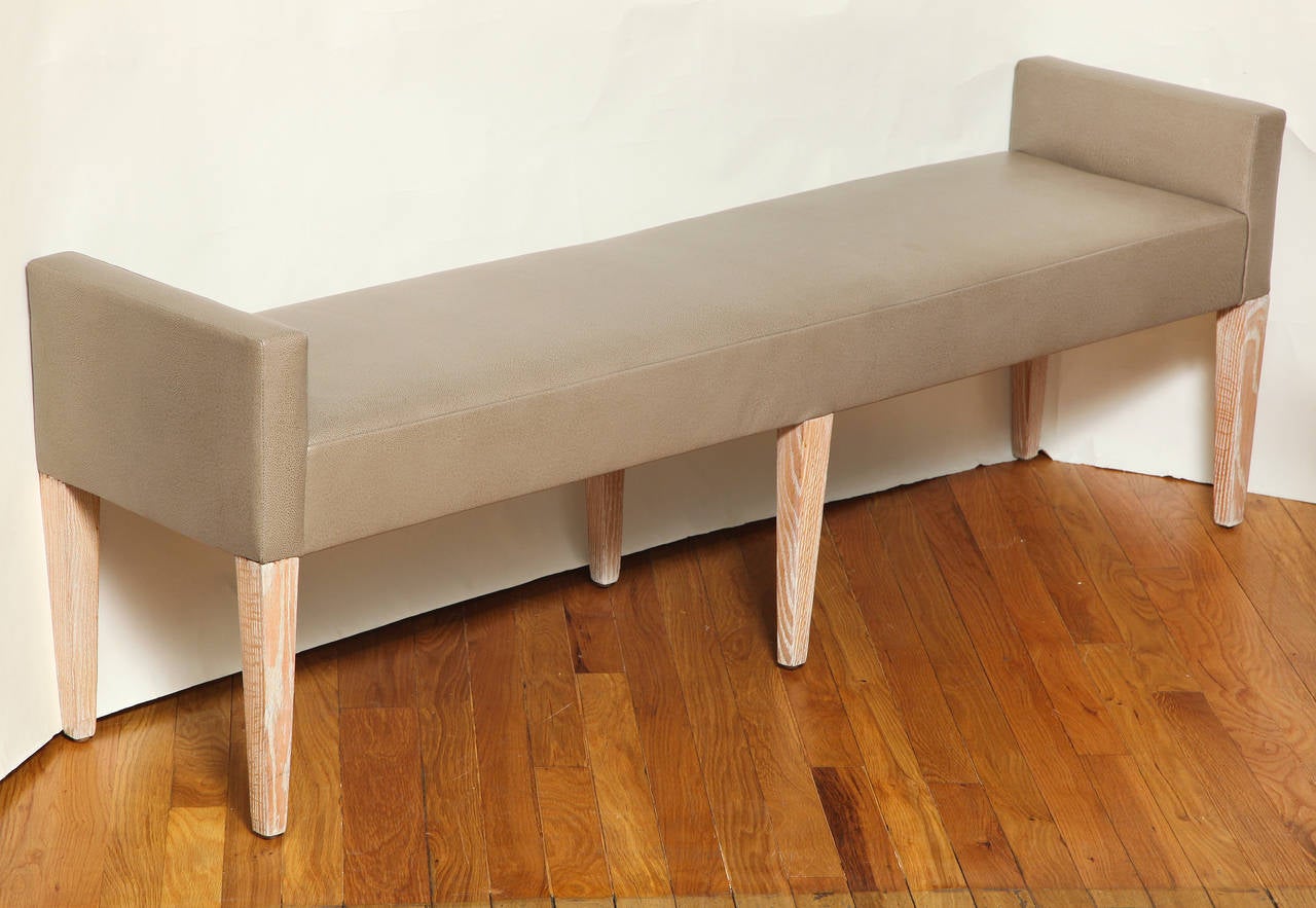 An American Mid-Century narrow bench with six square and tapering legs. The legs and apron with white cerused oak finish. The seat and raised sides upholstered in grey leather.