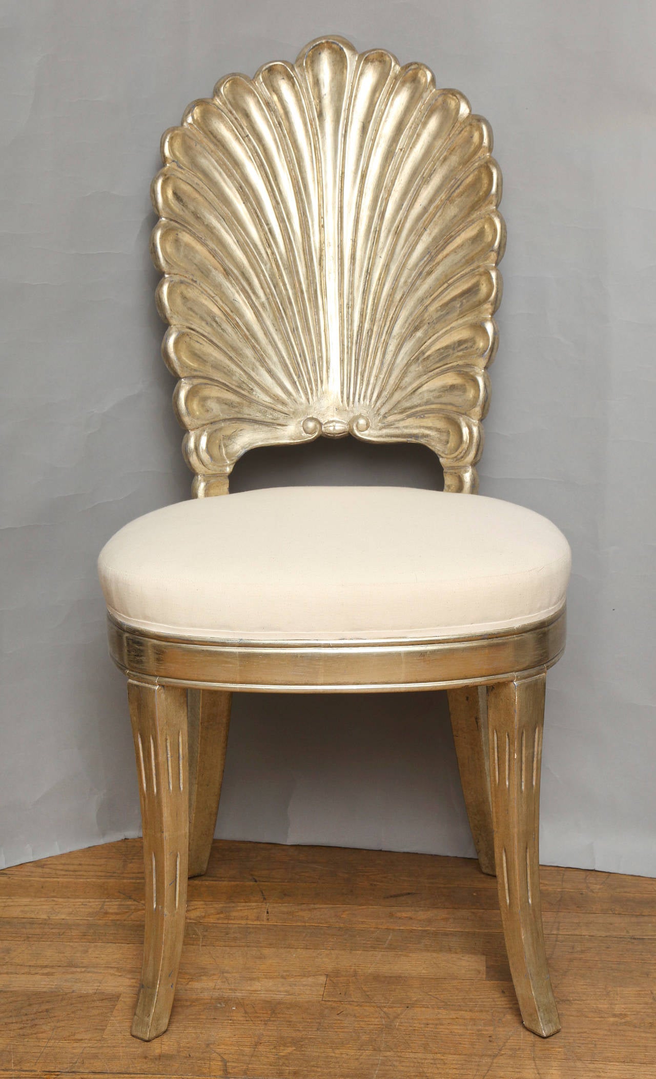 A shell back carved and white gold leafed chair having four sabre legs and upholstered seat. (7 available).