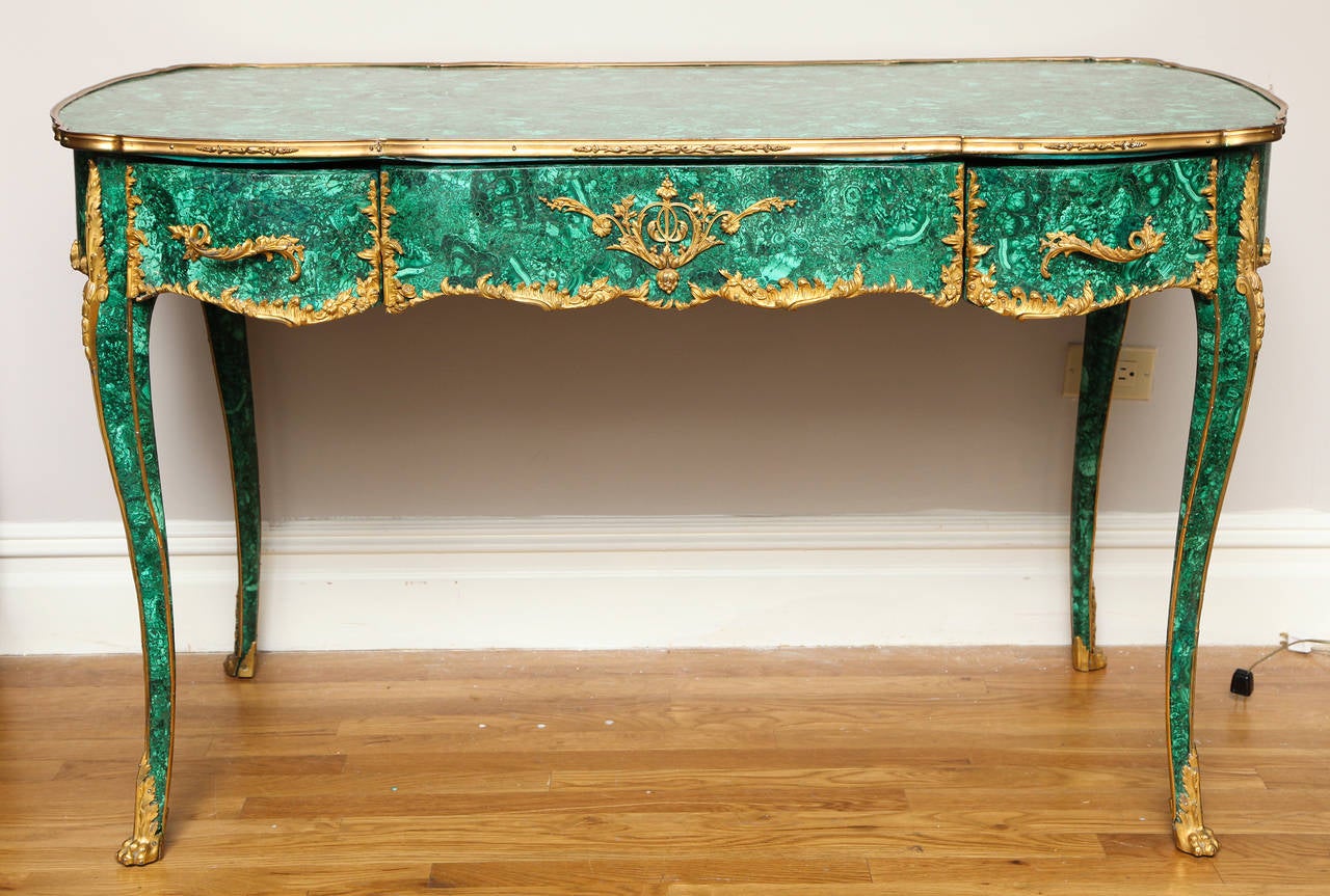 A French Regence style writing table finished on four sides with drawers and apron having gilt bronze mounts surrounding drawer fronts, gilt bronze pulls, and sabots. The flat top having shaped sides trimmed with gilt bronze edge. Each cabriole leg