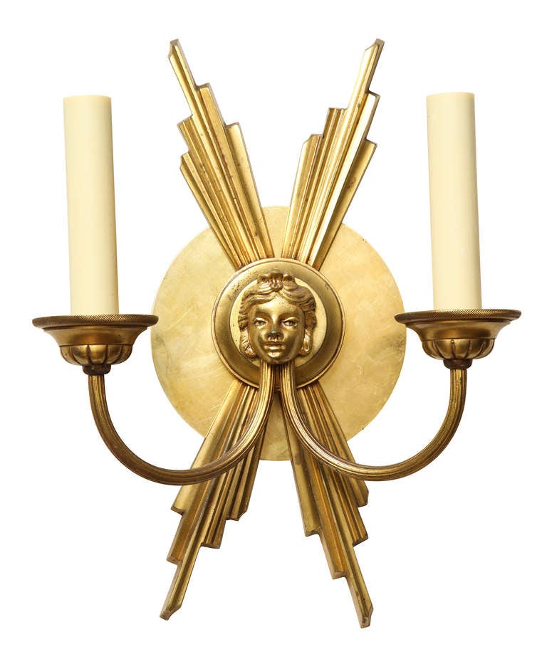 A pair of two-light French wall sconces the back in the form of sunrays with a mask motif center.