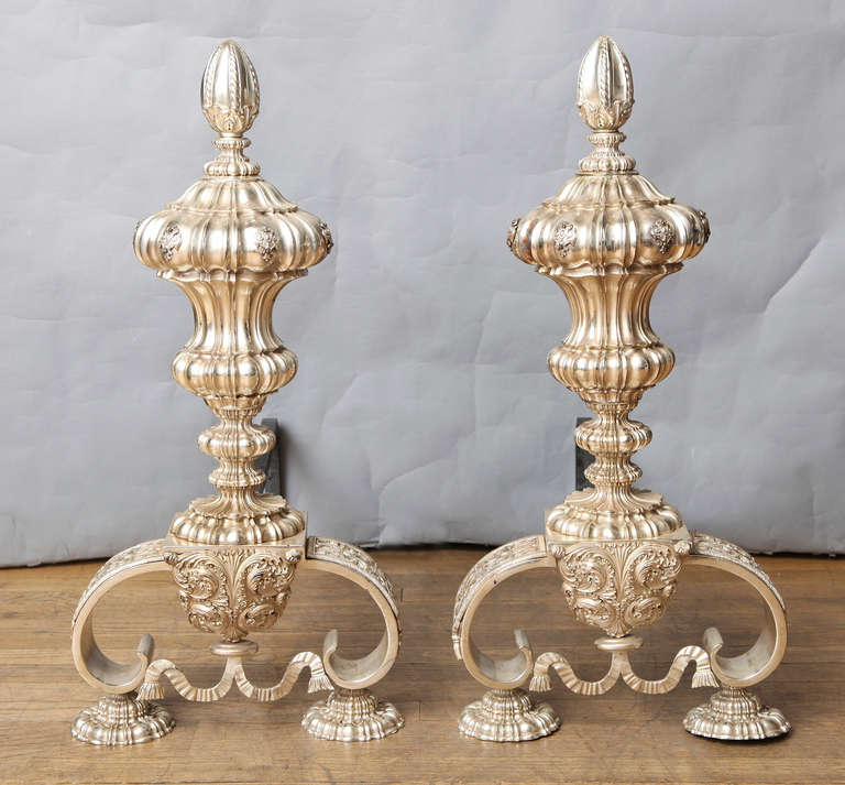 A pair of silver-nickel plated bronze Caldwell andirons in the form of vases with oversized finials on bracket feet with egg and dart molded detail. The lower section with trompe l'oeil swag and tassel motif.