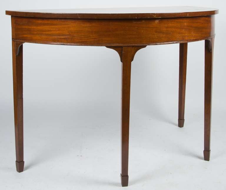 A pair of English mahogany demilune consoles with square and tapered legs.