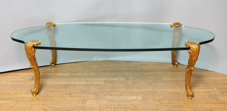 A glass top coffee table with chased gilt bronze cabriole legs and scalloped edge oval top signed by New York maker P.E. Guerin.