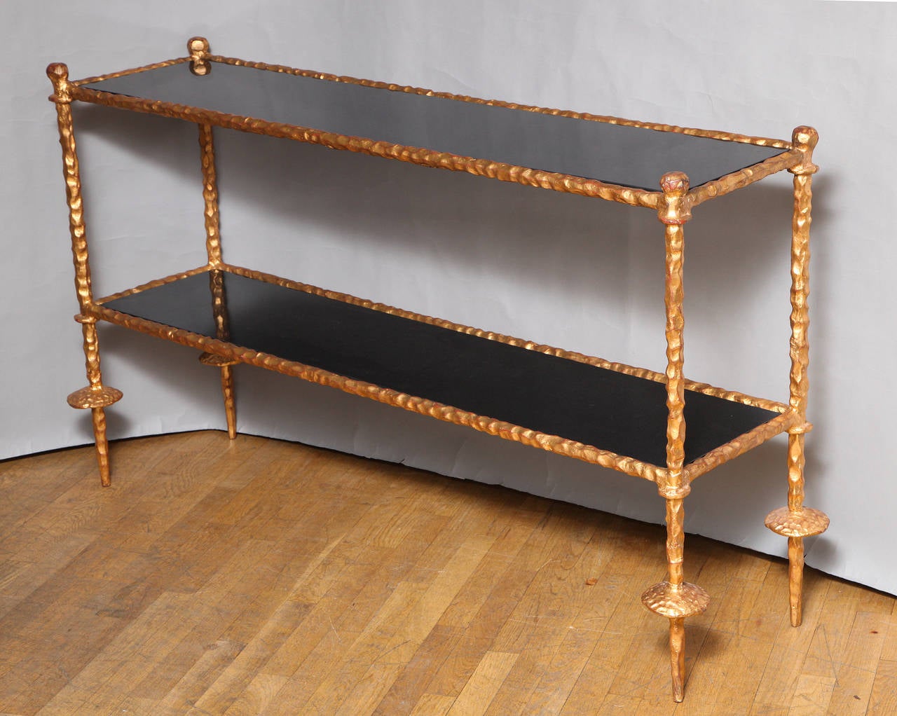 A two tiered gilt iron Giacometti style sofa table/étagère with polished black granite surfaces.
