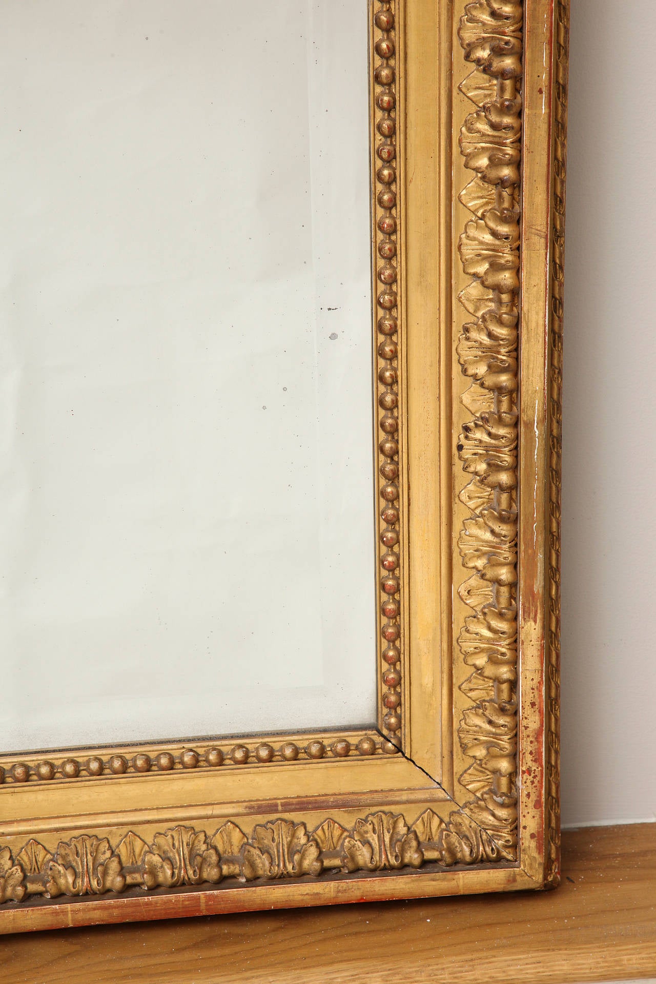 An oversized French Empire style mirror, the antique beveled rectangular glass framed by carved giltwood and gesso frame with beadwork, leaf tip, and rope twist moldings.
