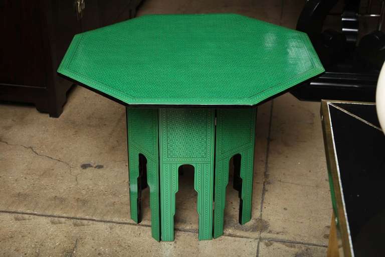 A green lacquered octagonal side table with decorative details in black and gold. Foldable base.