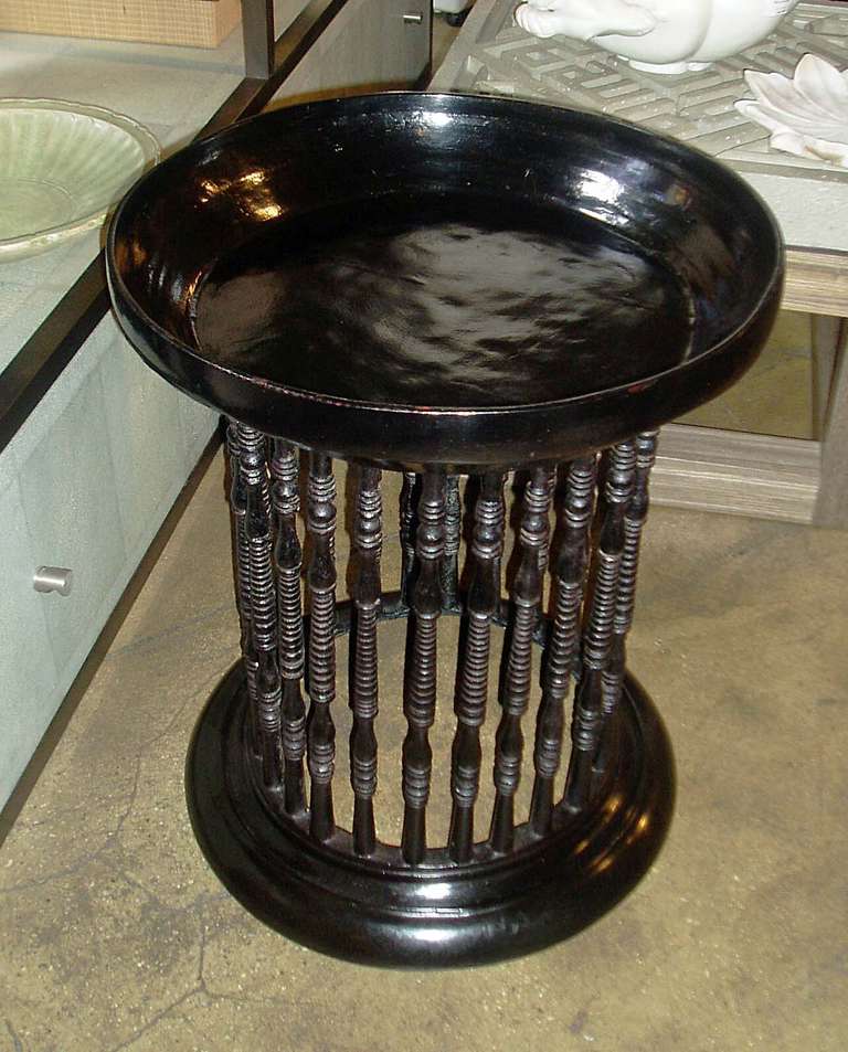 A black lacquered round teakwood side table with spindled base.