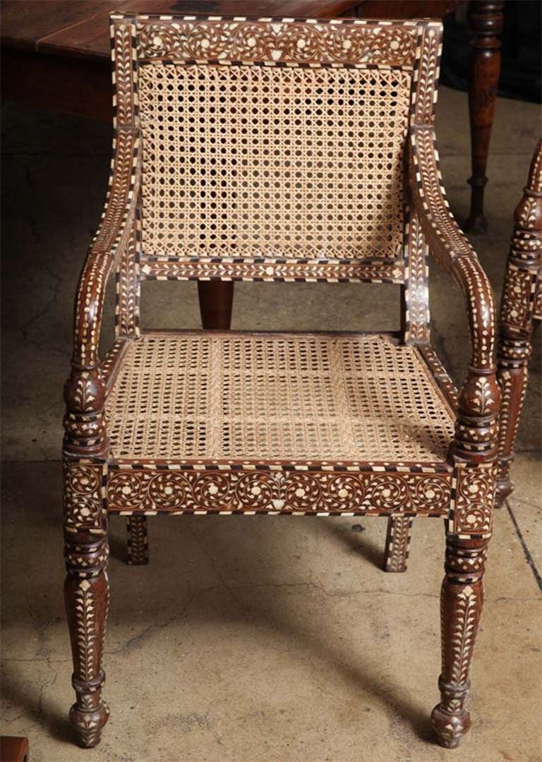 A wooden armchair with cane seat and square top back. Bone inlays in a classic pattern throughout, from India.