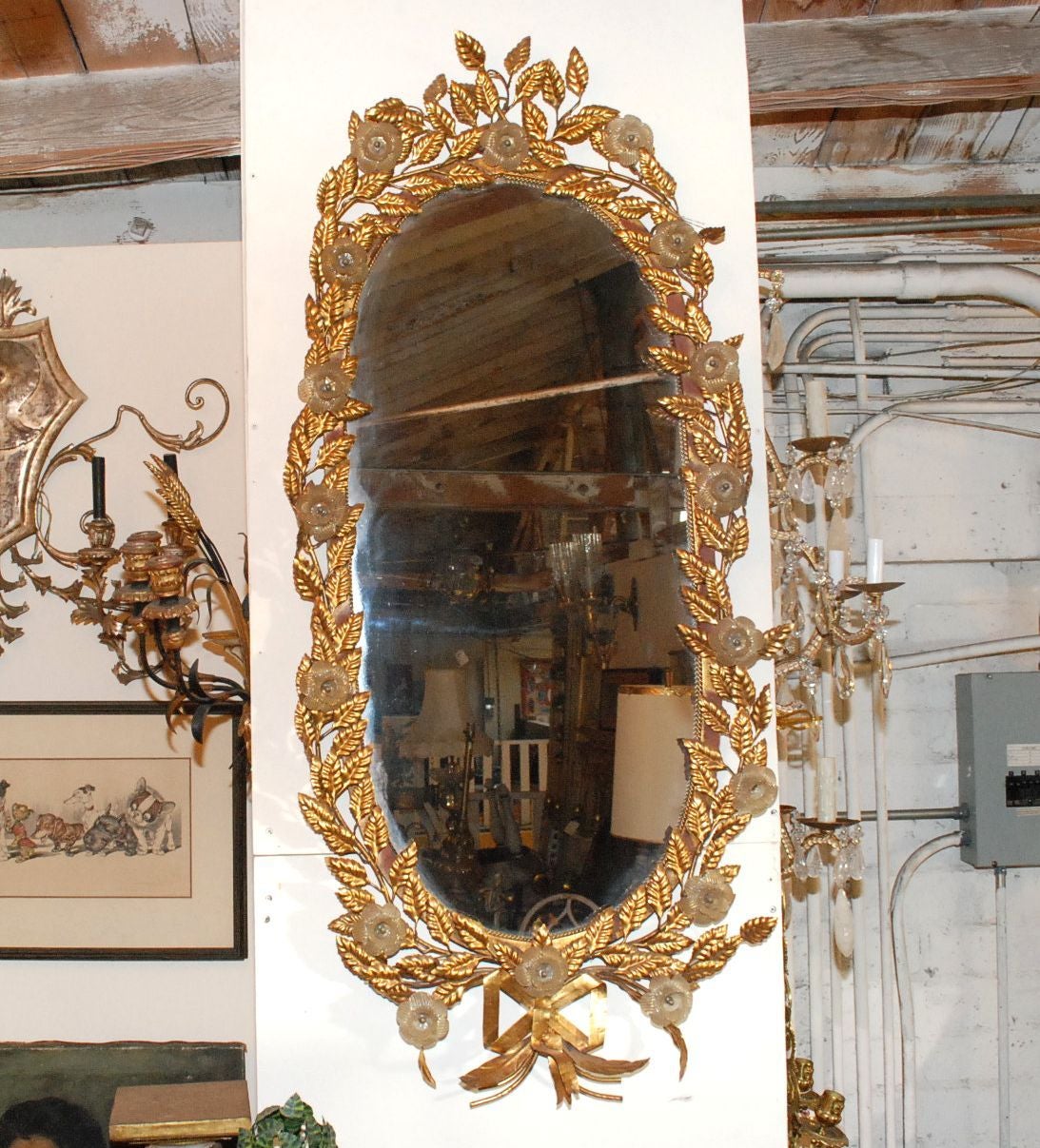 Un extravagant miroir en tole doré et verre de Murano. Le miroir est entouré de feuilles dorées et décoré d'une guirlande de rubans à la base. Des fleurs en verre de Murano accentuent les feuilles.