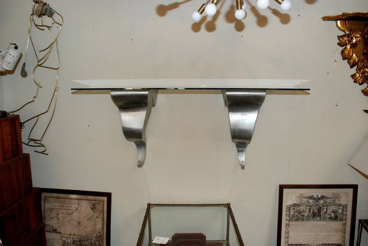 A unique aluminium and glass wall shelf by Michael Aram. Signed and dated 1993 on one of the aluminium wall mounts. There is a tiny hole near the bottom on one of the wall mounts (see 2nd to the last photo).

Measurement with glass shelf is 60
