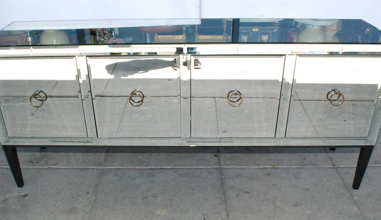 An elegant mirrored credenza or buffet. Has four doors with brass handles. Mirror is beveled. There are two tiny chips in mirrored front (one on a door edge and the other on a side panel in the front) that are hardly noticeable but mentioned for