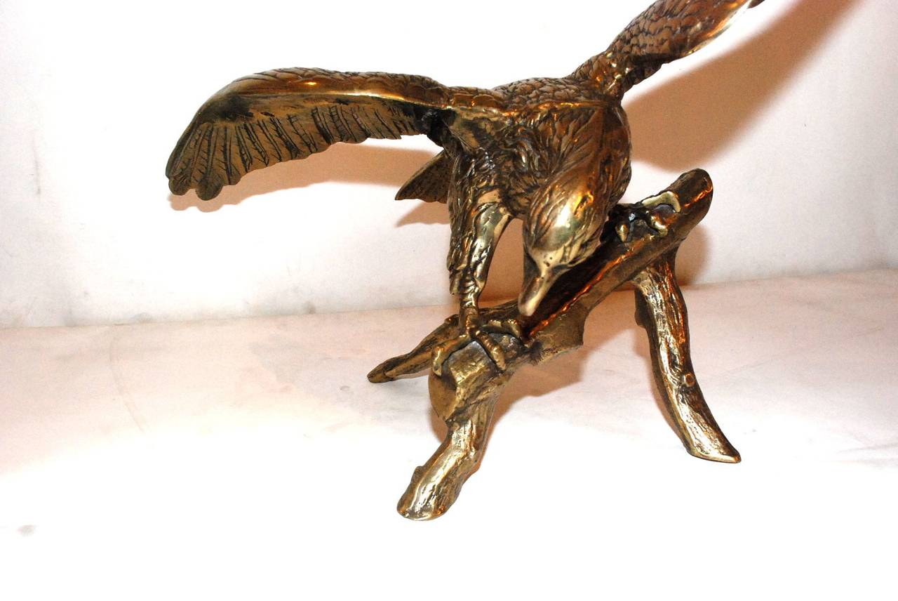 An amazing Mid-Century brass eagle. It is perched on a tree branch with wings spread out.