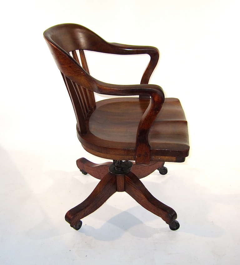 This swivel desk armchair of solid walnut is styled after the British Bankers Chair and manufactured by the SIKES Co. of Philadelphia, PA. The seat height and back tension is fully adjustable. This chair offers a generous seating area and is one of