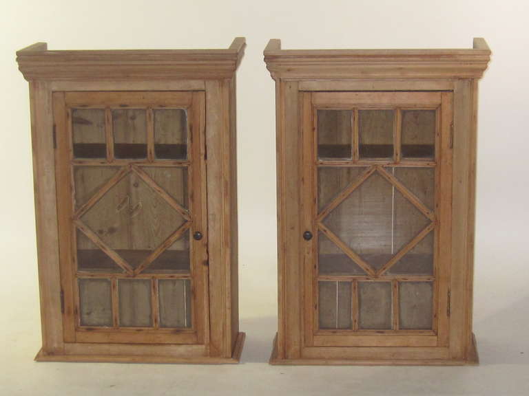 A pair of mid nineteenth century pine cabinets from Ireland. The single door opening  is glazed and  two interior shelves.