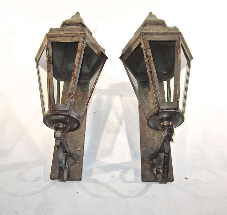 A pair of Iron and tole early outdoor lanterns with original iron mounting backplate. These are not electrified and still have the gas jet tubing. A handsome pair ready to join the 21st century lighting needs or as decorative objects.