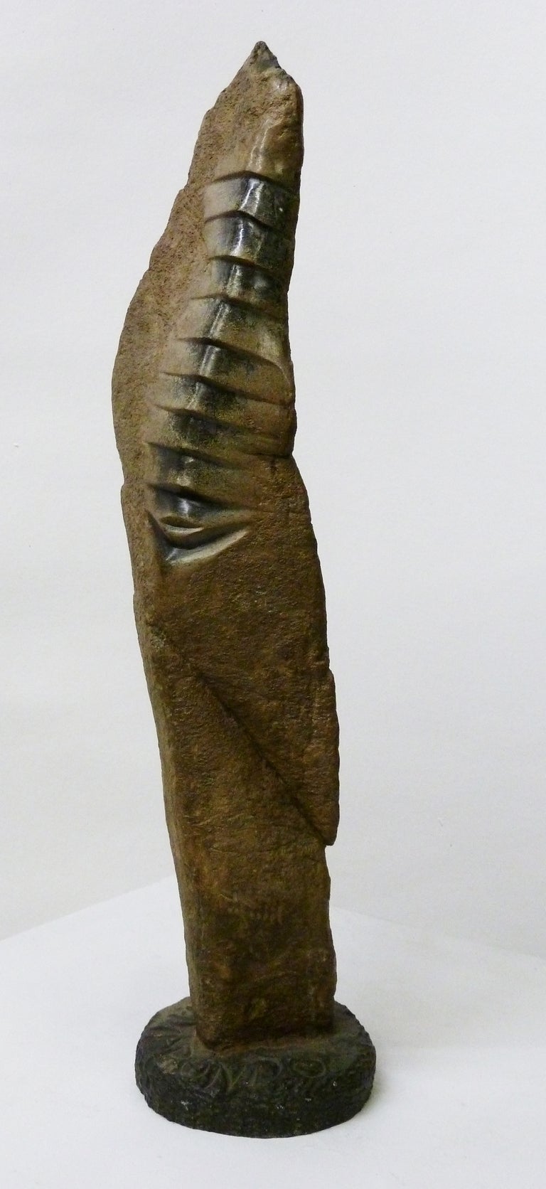 This evocative sculpture by famed Zimbabwe artist Wilbert Mapundo features rough stone juxtaposed by smoothly finished suture or vertebrae-like marks along the side. It is signed at the base.