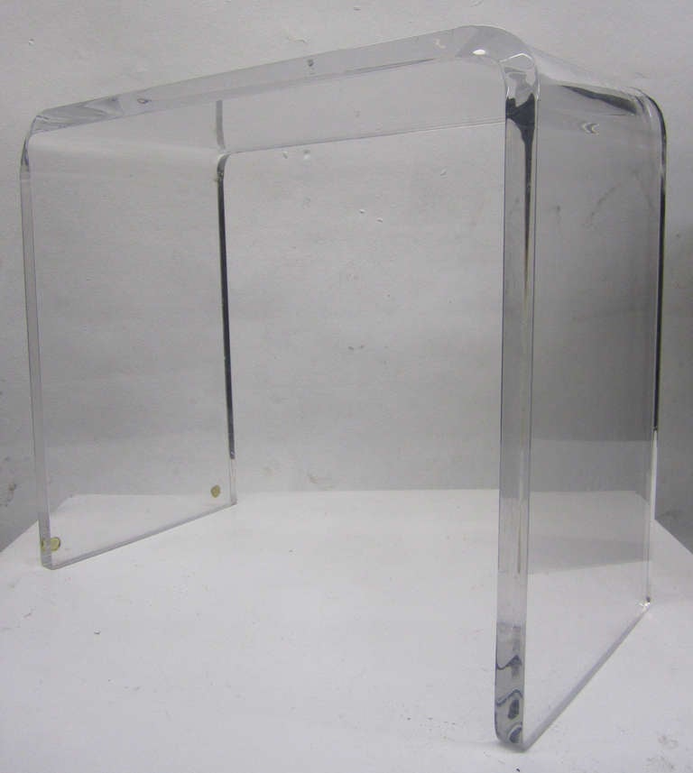 This waterfall side table is comprised of a single piece of Lucite. The table may be displayed resting on both legs or flipped on its side in a 'C' shape.