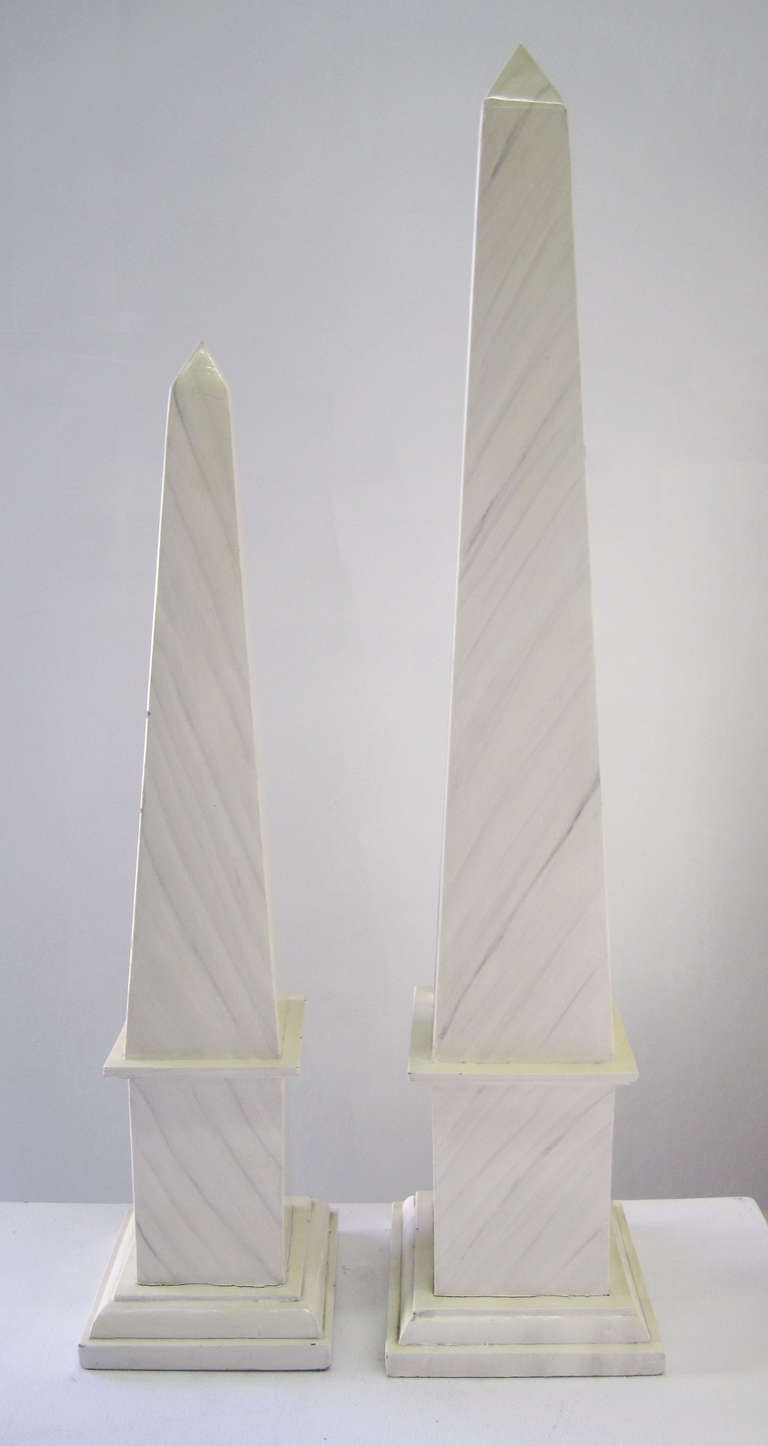 Pair of obelisks rendered in wood and painted with a faux marble finish. The separate, matching pair can be displayed separately or side-by-side. 

The smaller obelisk measures 6.38