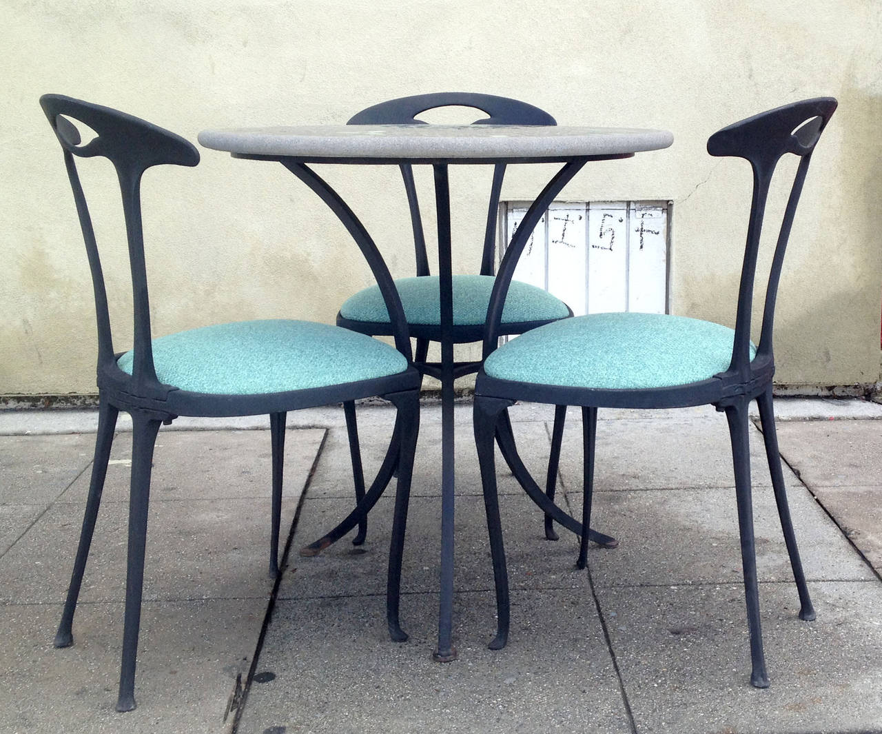 This patio set features three chairs and a petite mosaic top table. They are made of cast iron. The circular mosaic table top is supported by a three-legged iron base with an elegant shape. 
Table measures 29