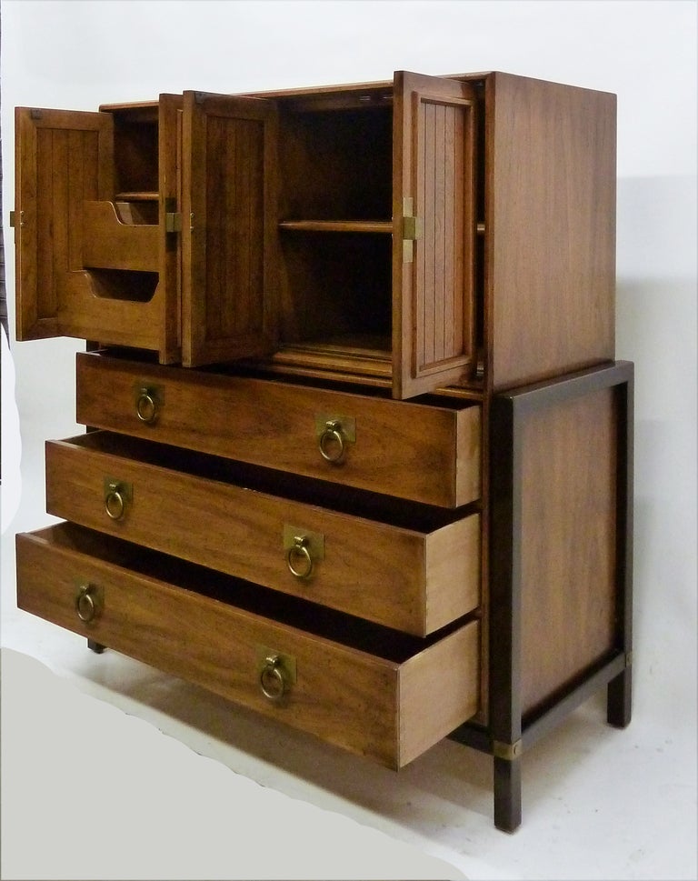 Henredon high boy in distressed walnut wood. Bottom half sits on a darker wood frame with brass detaiingsl on legs. Solid brass hardware on drawers and cabinets. Storage shelves and drawers in top cabinets. The top drawers split in 3 compartments