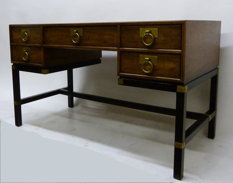 Henredon distressed walnut desk with solid brass drop ring pulls. Desk drawers are set atop a darker wood base with brass detailing.
It is finished on all sides with insert panels in the back. Original matching caned chair is included  18 w x 17.5