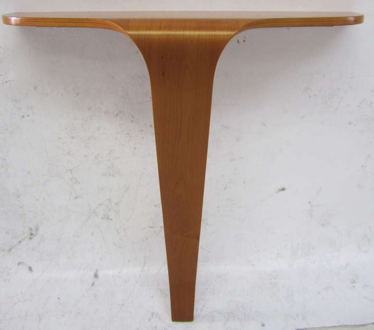 This minimal console table in walnut plywood is wall-mounted and supported by a single leg which flares slightly at the base. Reminiscent of Scandinavian designers such as Alvar Aalto. Perfect for a compact setting.