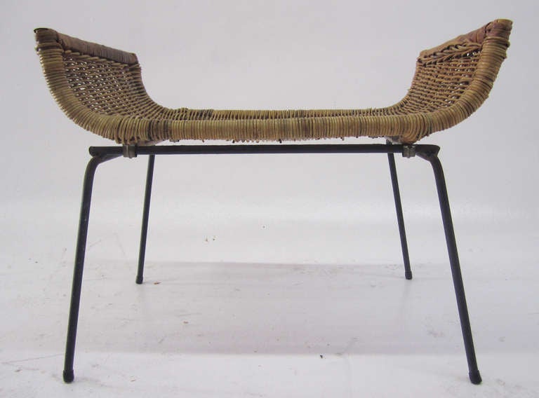 This petite stool or bench originally designed by Danny Ho Fong is comprised of a curved woven rattan surface and a cast iron frame. Tropi-Cal, a rattan and wicker furniture company founded by Fong and brother Muey, has expanded into Fong Brothers