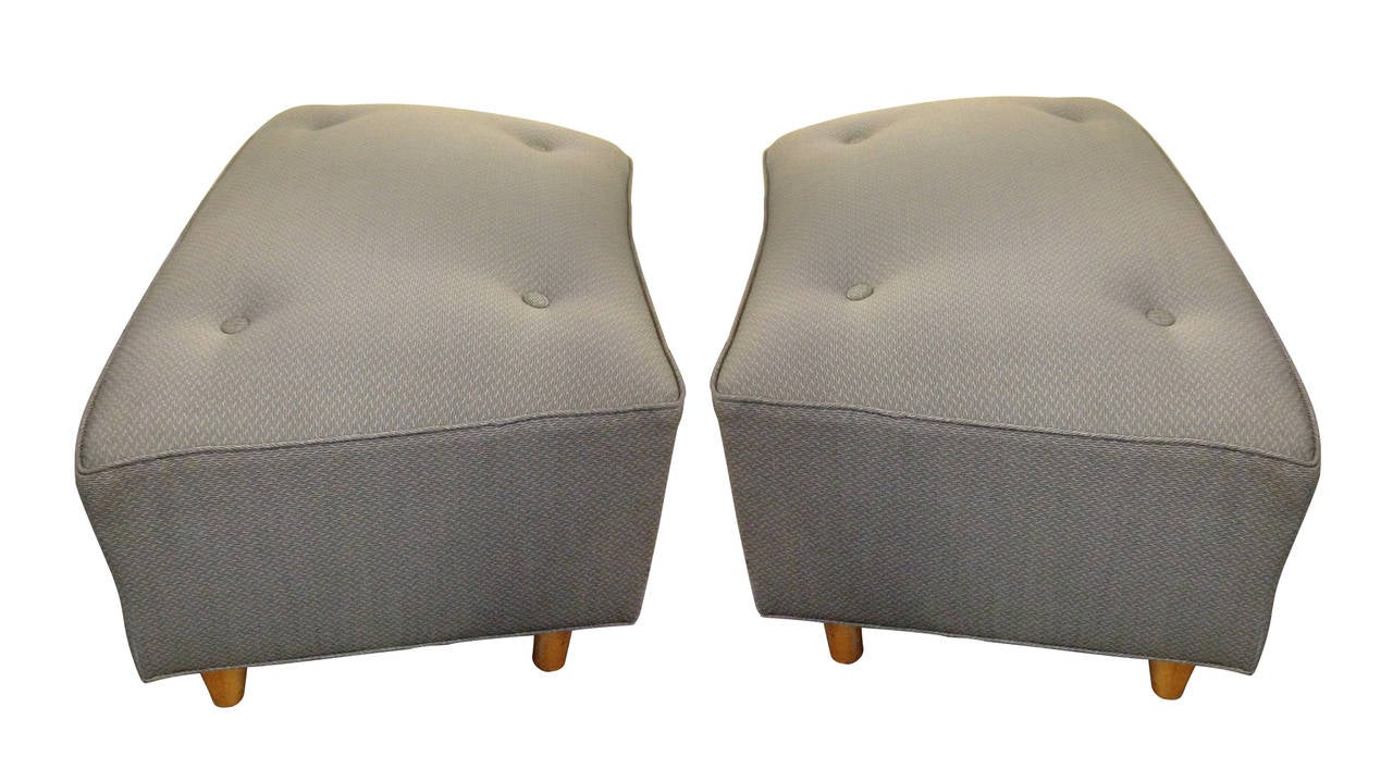 This pair of trapezoidal ottomans features a slightly curved cushion each supported by four tapered blonde wood legs. The functionality and elegant simplicity of this design coupled with the blonde wood used make you recognize the products of