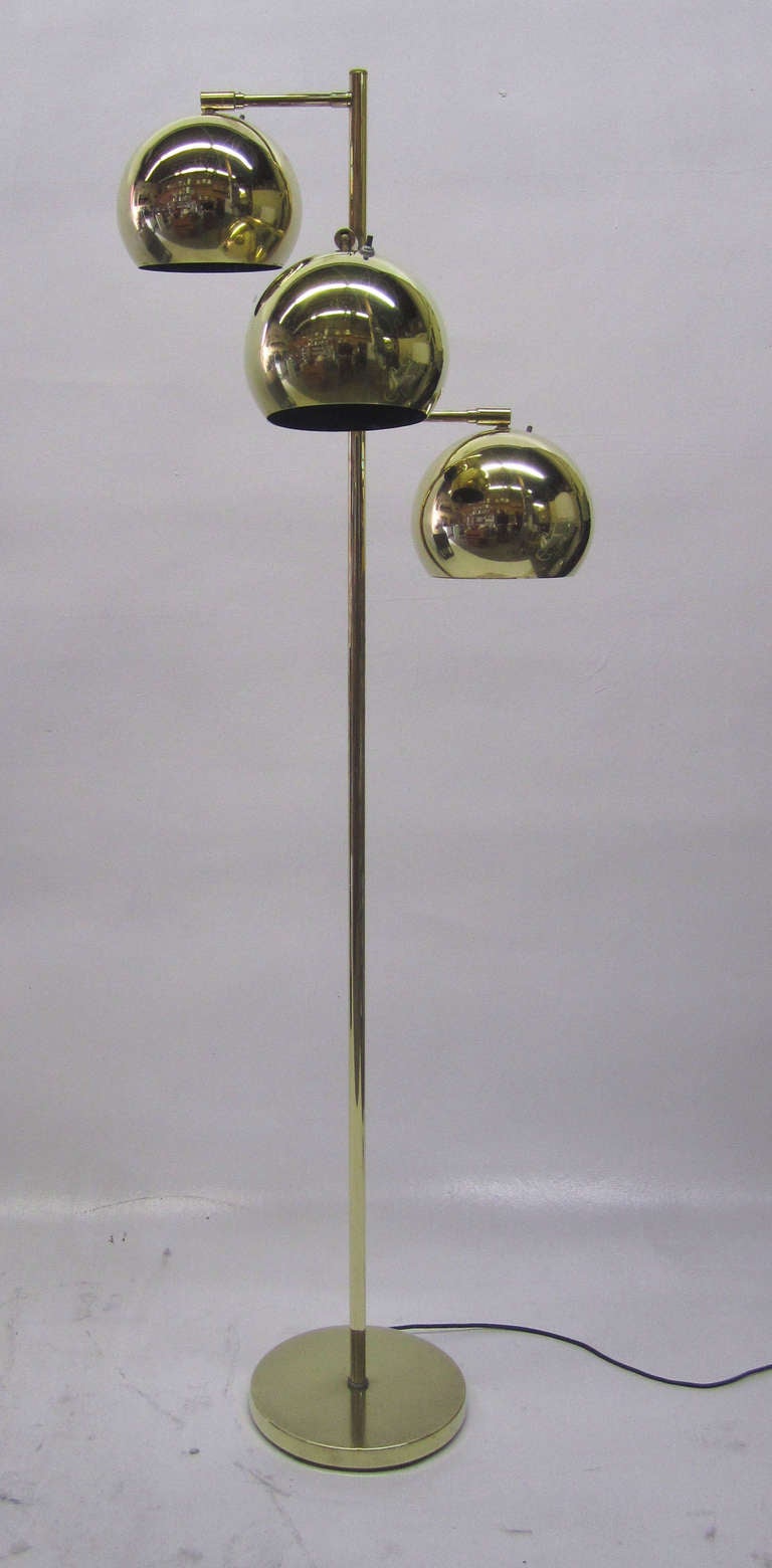 This brass floor lamp features three large globes at varying heights. Each fixture has an individual on / off switch and may be rotated independently. The spine of the lamp is circular as is the base.