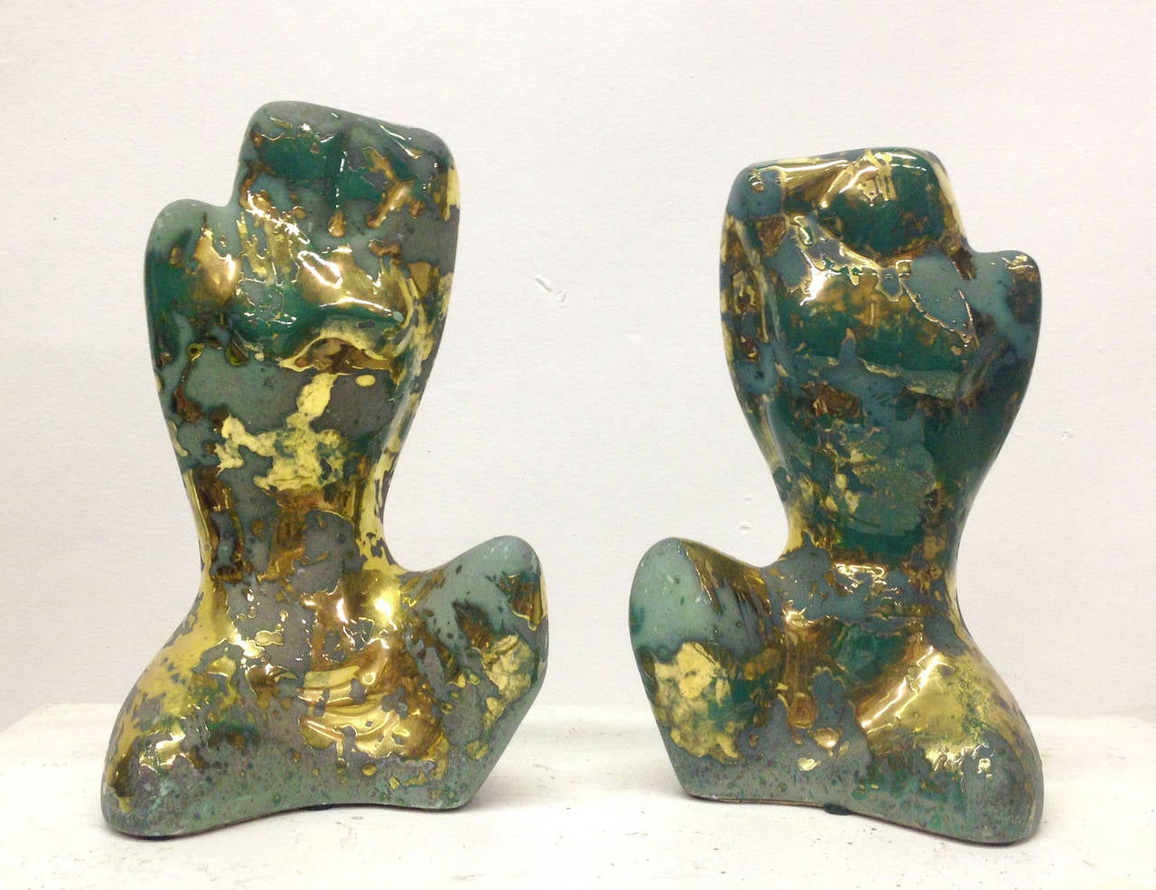 A pair of sculptures depicting a man and woman's bodies rendered in a classical fashion in modern materials. Each ceramic piece has a unique glaze that resembles oxidation and dripping gold. 
The sculpture of the woman measures 5.75