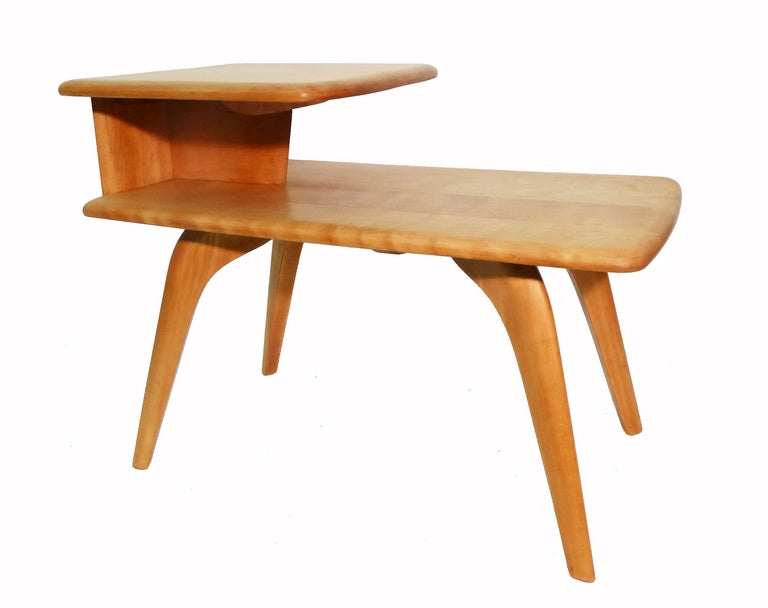 These elegant mid-century modern side tables made of solid maple  were manufactured by Heywood Wakefield. The tables feature two-tiered surfaces and are supported by graceful arcing legs.
Heywood Wakefield's stamp appears on underside (see image 9).