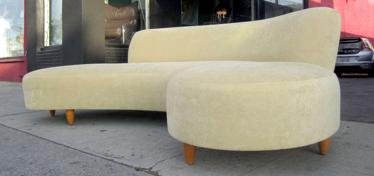 The style of this curved sofa resting on tapered wooden dowel legs is very reminiscent of mid-century modern master Vladimir Kagan. The piece has recently been reupholstered in a soft yellow chenille microfiber.
