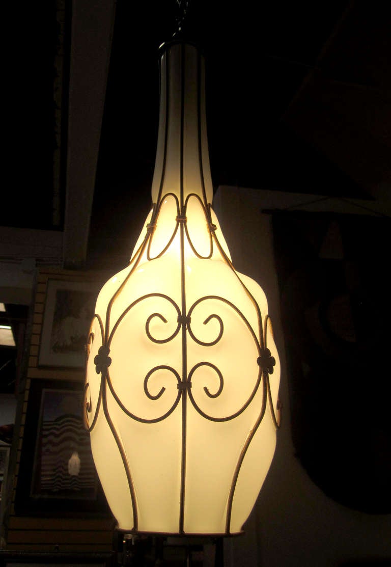 This Murano pendant features a hand blown glass body which perfectly fits a brass frame with curled, nature-inspired motif. When lit, the opaque white glass turns a soft yellow against the brass cage.