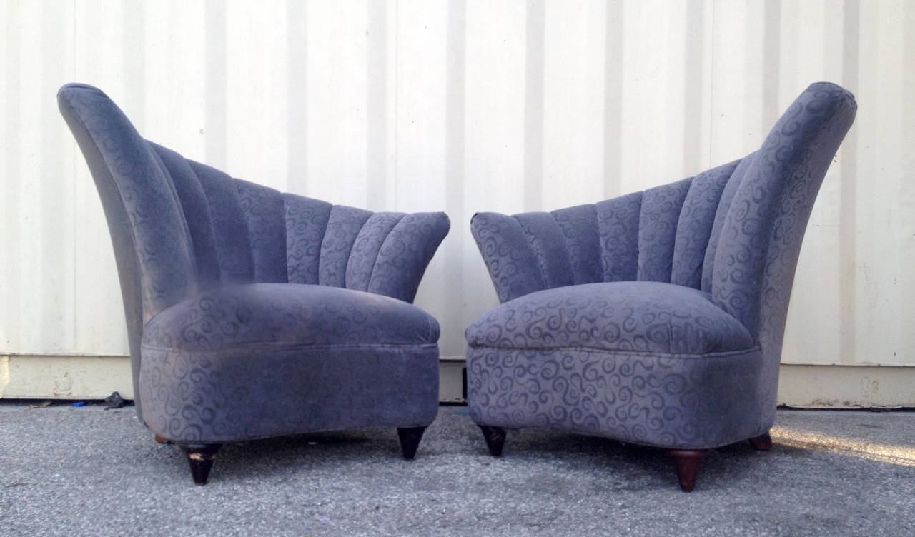 This pair of asymmetrical lounge chairs feature a sloped, scalloped back rest and comfortable overstuffed seat. These chairs retain their original grey/blue velours upholstery with a subtle swirling pattern.
They stand on conical feet.